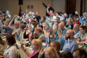 Forsa members at conference holding up their hands and badges to vote on motions.