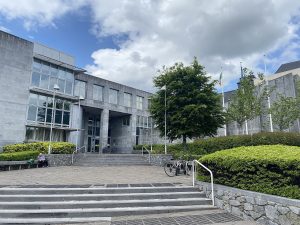 Photo of Galway County Council building. It is a grey brutalist building with a large stepped forecourt flanked by trees and shrubs.